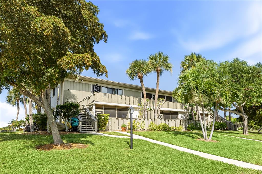 A two-story apartment building with a wooden staircase and palm trees on a grassy lawn — 6500 FLOTILLA DRIVE UNIT 235, HOLMES BEACH, FL