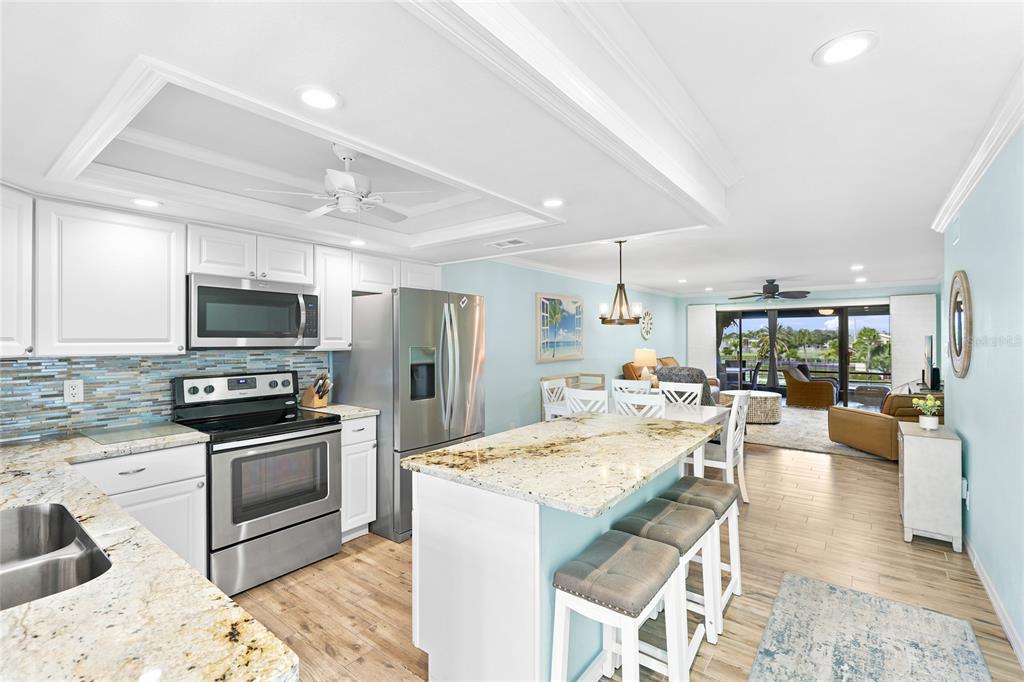A kitchen with white cabinets and granite countertops overlooks a dining area and living room — 6500 FLOTILLA DRIVE UNIT 235, HOLMES BEACH, FL