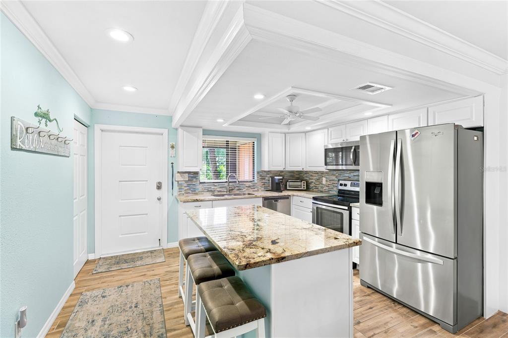 A kitchen features a granite-topped island, stainless steel appliances, white cabinetry, and light blue walls — 6500 FLOTILLA DRIVE UNIT 235, HOLMES BEACH, FL