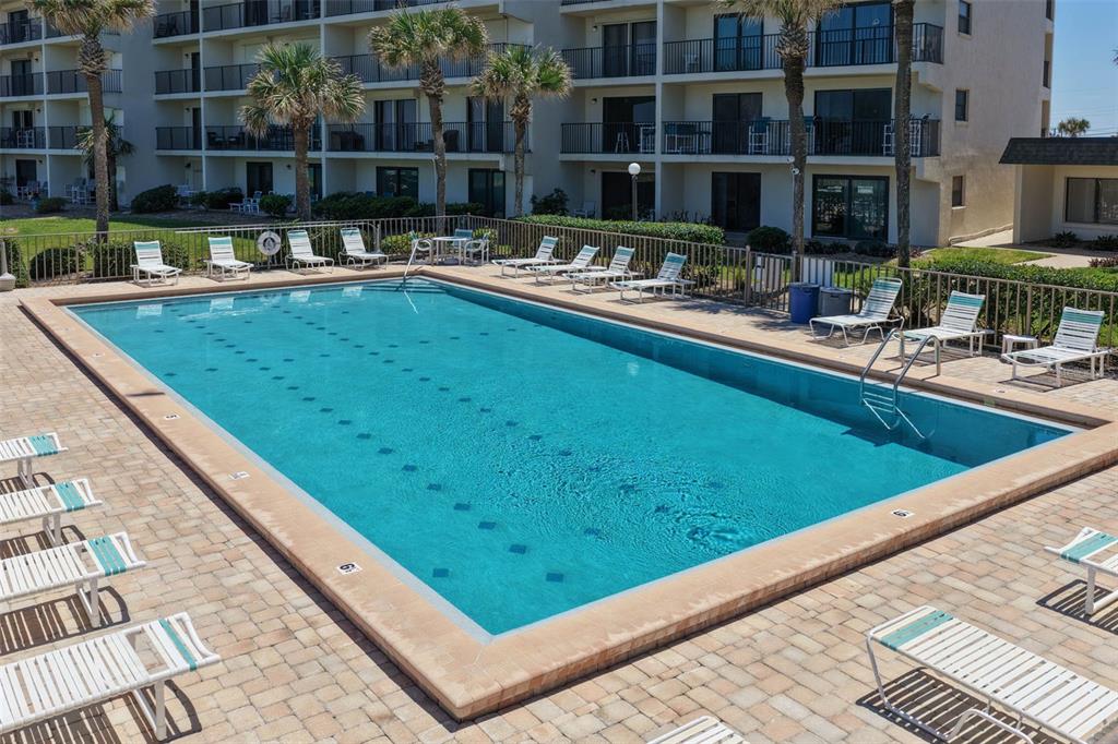 An outdoor rectangular swimming pool is surrounded by a paved deck with numerous lounge chairs — 2700 OCEAN SHORE BOULEVARD UNIT 316, ORMOND BEACH, FL