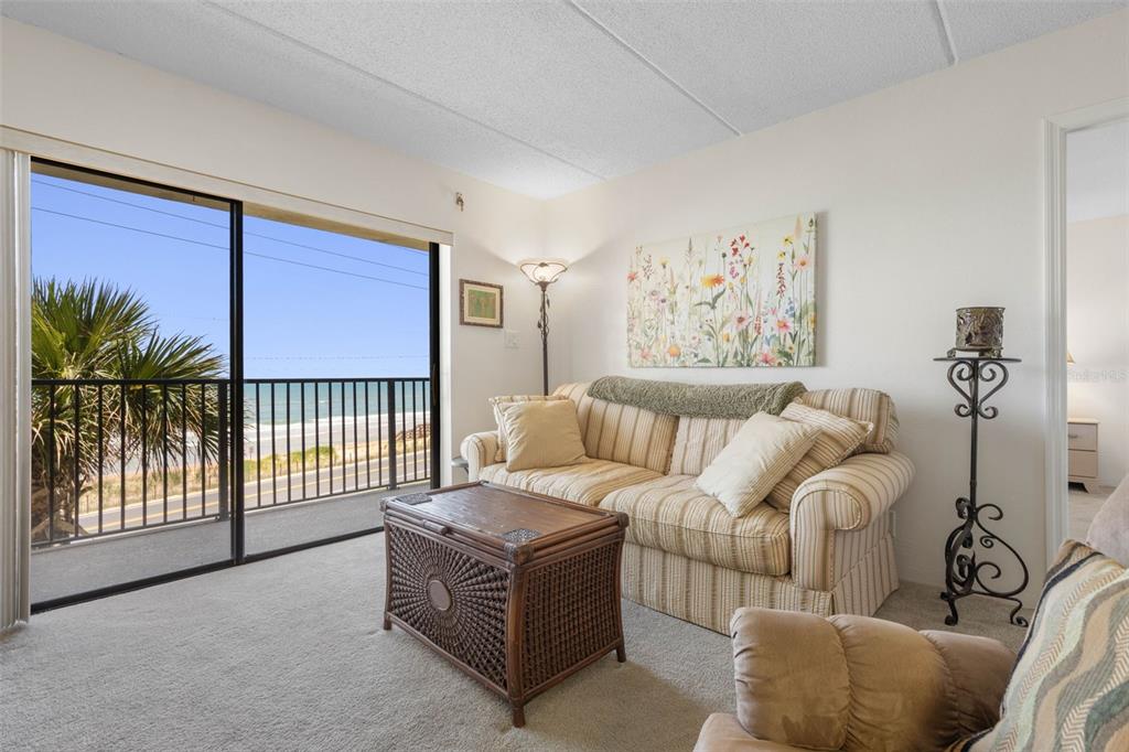 A living room with a striped sofa, wicker coffee table, and a balcony overlooking the ocean — 2700 OCEAN SHORE BOULEVARD UNIT 316, ORMOND BEACH, FL