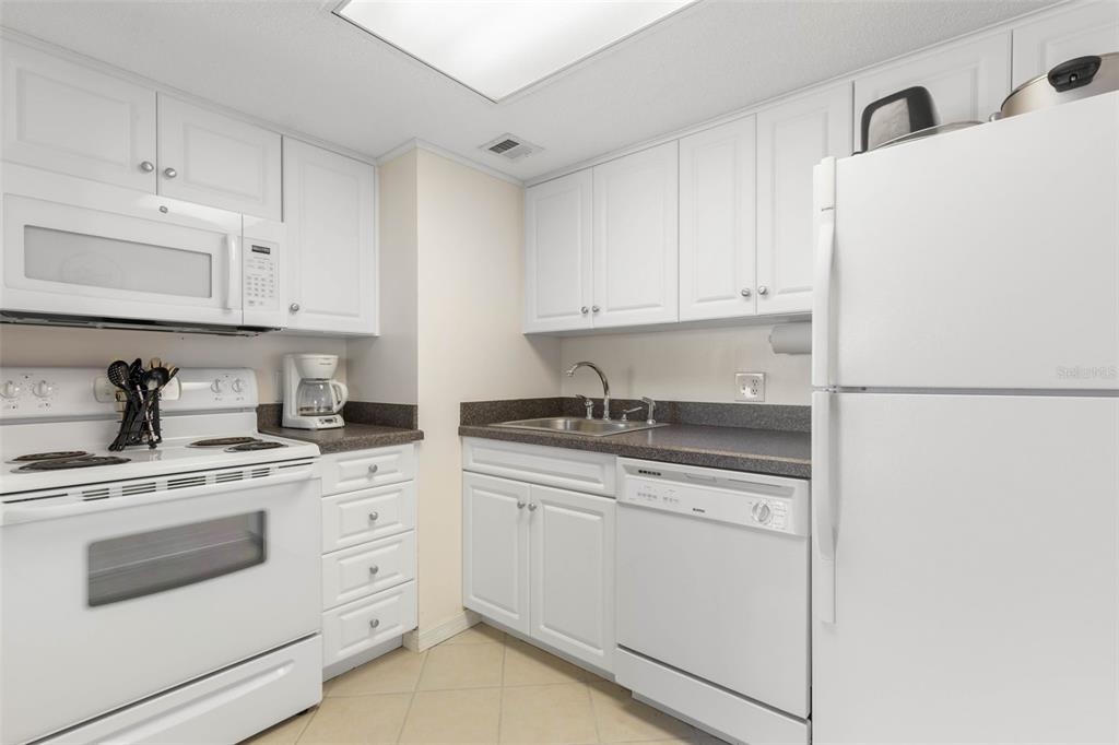 A kitchen features white cabinets, white appliances, dark countertops, and a tiled floor — 2700 OCEAN SHORE BOULEVARD UNIT 316, ORMOND BEACH, FL