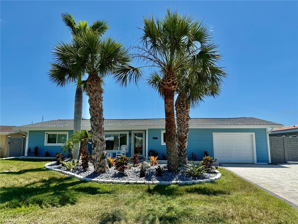 A light blue single-story house features a front garden with palm trees and a garage — 12300 4TH STREET E, TREASURE ISLAND, FL