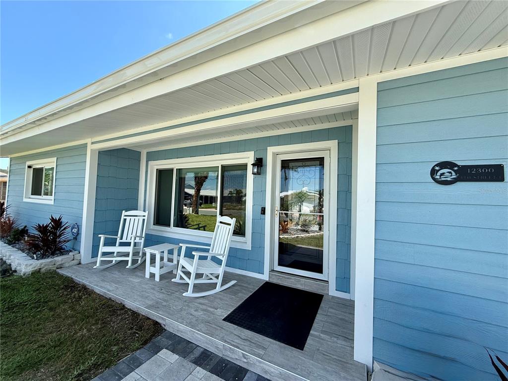 A light blue house exterior features a covered front porch with two white rocking chairs — 12300 4TH STREET E, TREASURE ISLAND, FL