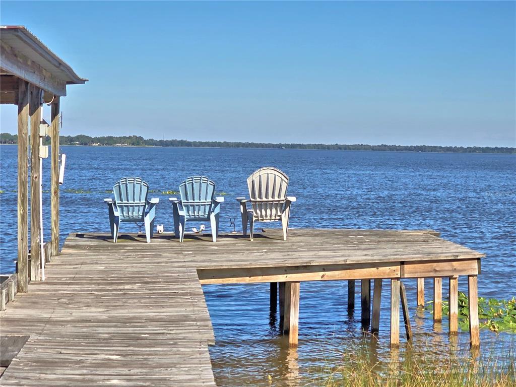 Three chairs sit on a wooden dock overlooking a large lake under a clear sky — 105 MAXCY LANE, FROSTPROOF, FL