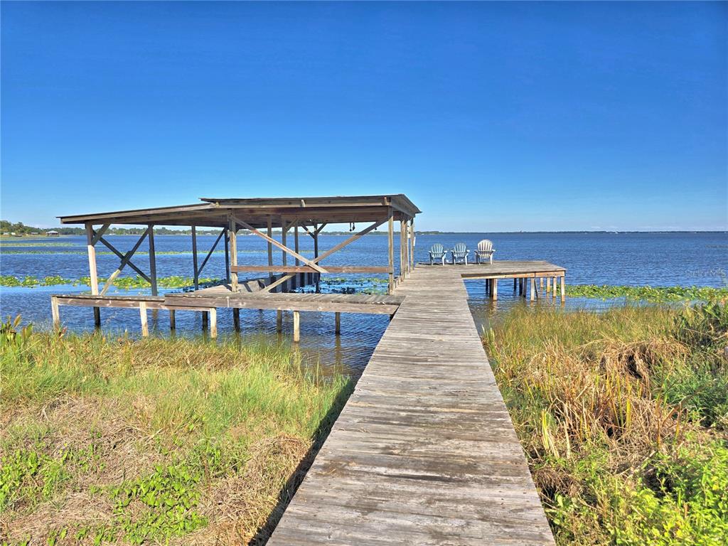 A wooden dock with a covered boat slip extends into a lake under a clear sky — 105 MAXCY LANE, FROSTPROOF, FL