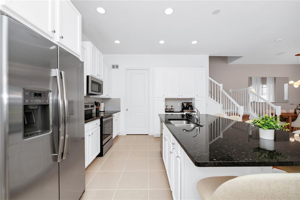 A modern kitchen features white cabinetry, stainless steel appliances, and a black granite island countertop — 302 CAPTIVA DRIVE, DAVENPORT, FL