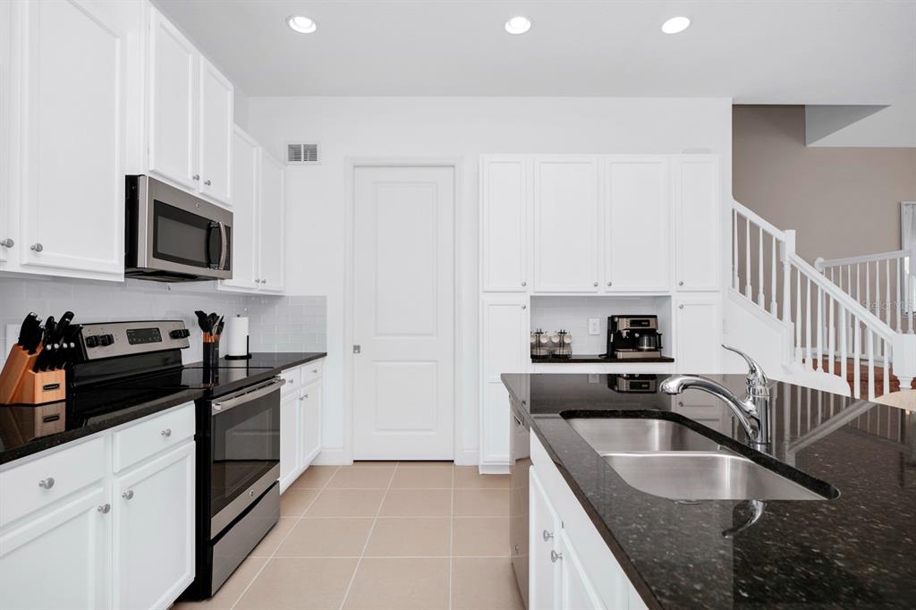 A modern kitchen features white cabinetry, black granite countertops, stainless steel appliances, and tile flooring — 302 CAPTIVA DRIVE, DAVENPORT, FL