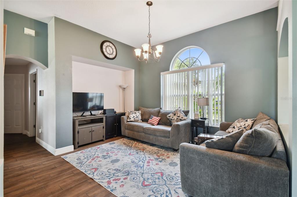 A living room features gray walls, a patterned area rug, two sofas, and a chandelier — 16920 FALCONRIDGE ROAD, LITHIA, FL