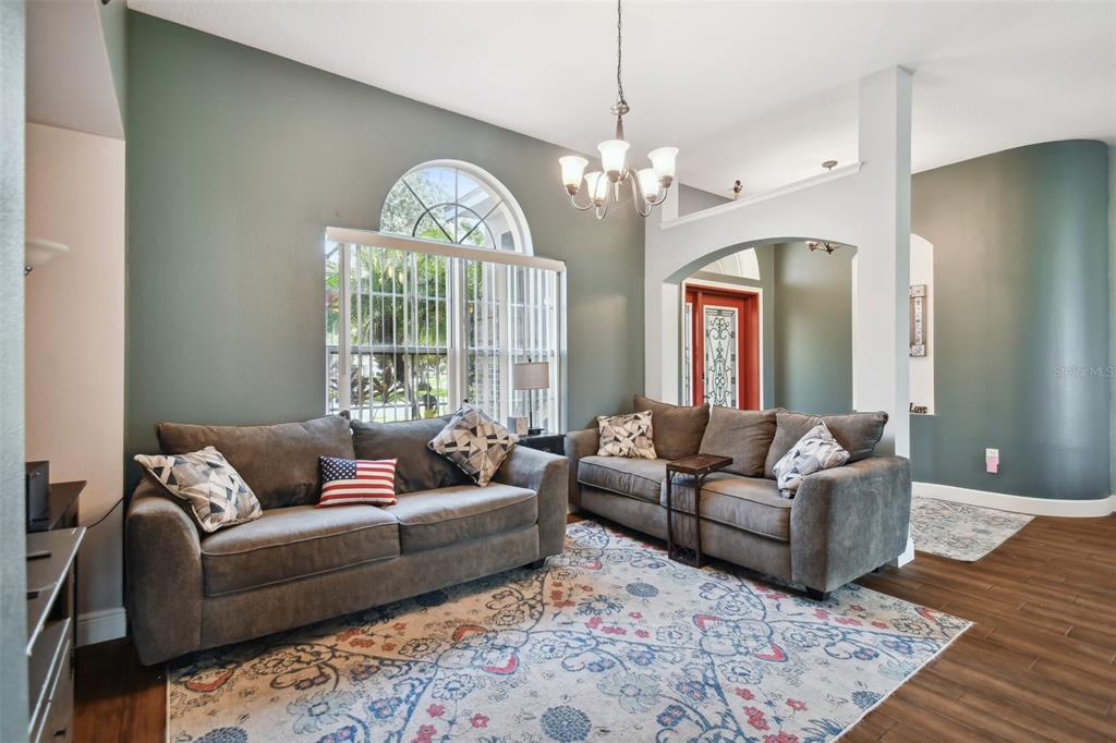 A living room features two gray sofas, a patterned area rug, and an arched window — 16920 FALCONRIDGE ROAD, LITHIA, FL