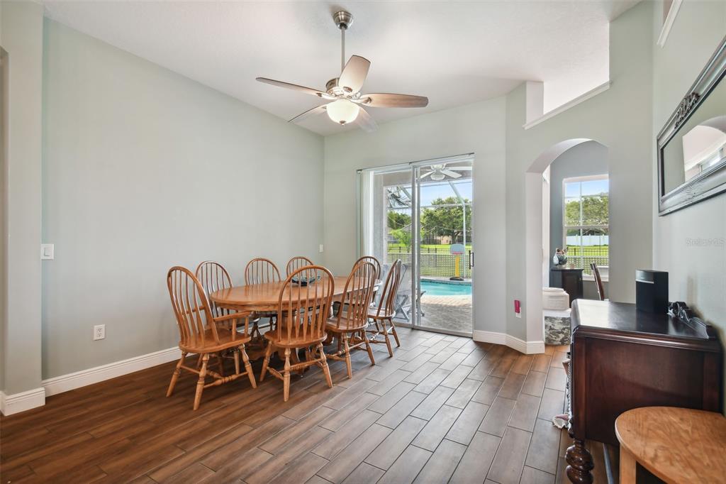 A dining room with wood-look tile floors, a wooden table, and a sliding glass door — 16920 FALCONRIDGE ROAD, LITHIA, FL