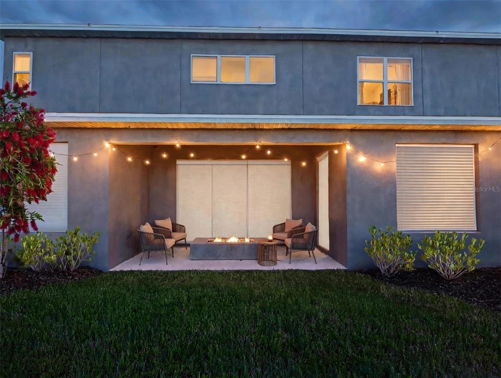 A backyard patio features a fire pit, outdoor seating, and string lights against a house exterior — 7228 BRADBURY CIRCLE, WESLEY CHAPEL, FL