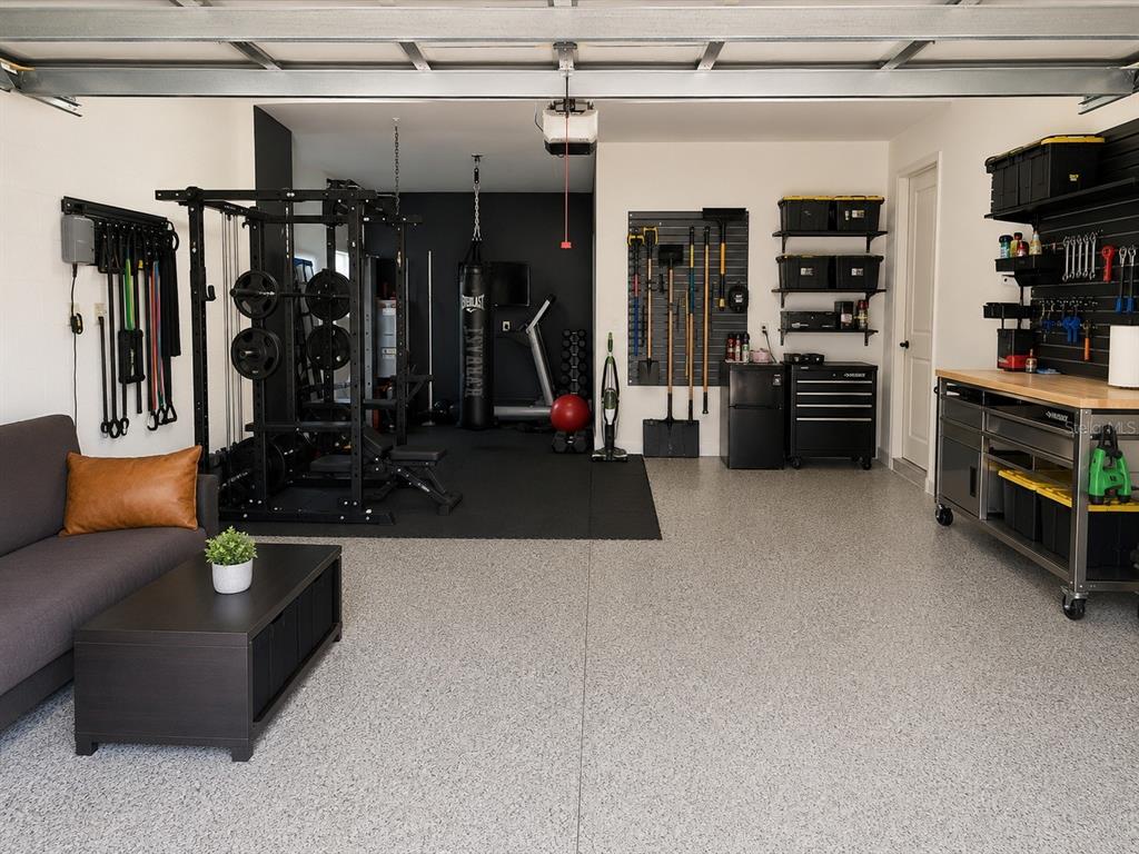 A garage converted into a home gym and lounge area with epoxy flooring and storage walls — 7228 BRADBURY CIRCLE, WESLEY CHAPEL, FL