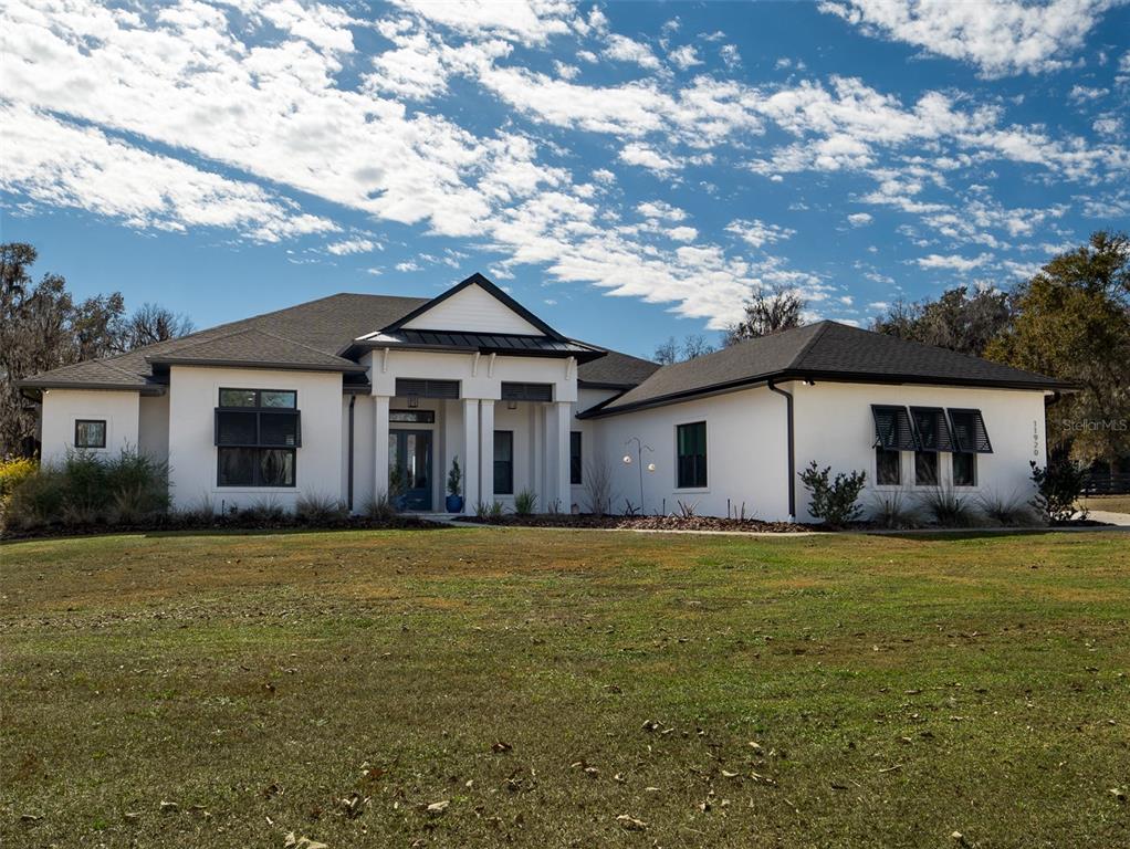 A white single-story house with a dark roof and black shutters sits on a lawn — 11920 SE 22ND AVE ROAD, OCALA, FL