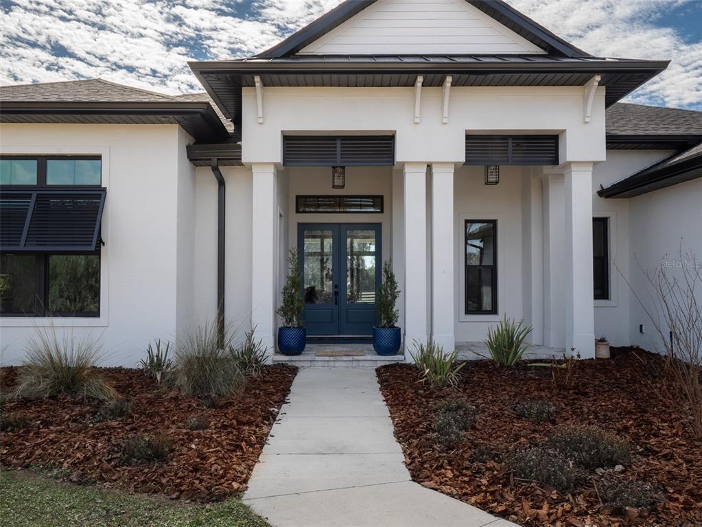 The exterior of a white house features a covered entryway with dark blue double doors — 11920 SE 22ND AVE ROAD, OCALA, FL