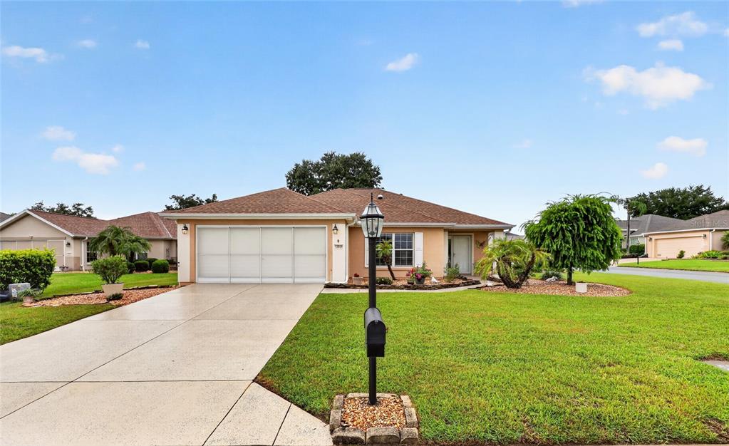 A single-story house with a tan exterior, a two-car garage, and a front lawn — 13806 SE 93RD AVENUE, SUMMERFIELD, FL