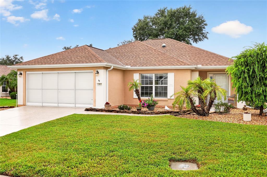 A single-story house with a tan stucco exterior, brown shingled roof, and a two-car garage — 13806 SE 93RD AVENUE, SUMMERFIELD, FL