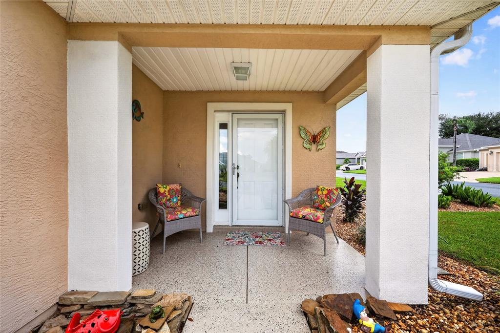A covered front porch features two wicker chairs, a white door, and decorative wall accents — 13806 SE 93RD AVENUE, SUMMERFIELD, FL