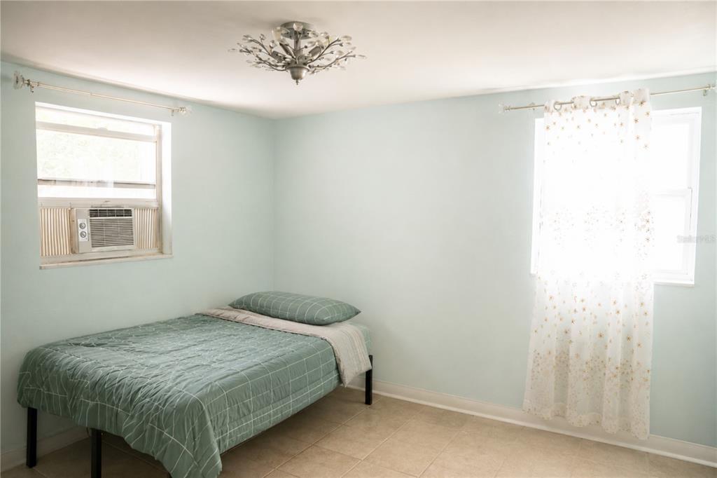 A bedroom with light blue walls, tile flooring, a bed, and two windows — 638 DOGWOOD COURT, DUNEDIN, FL