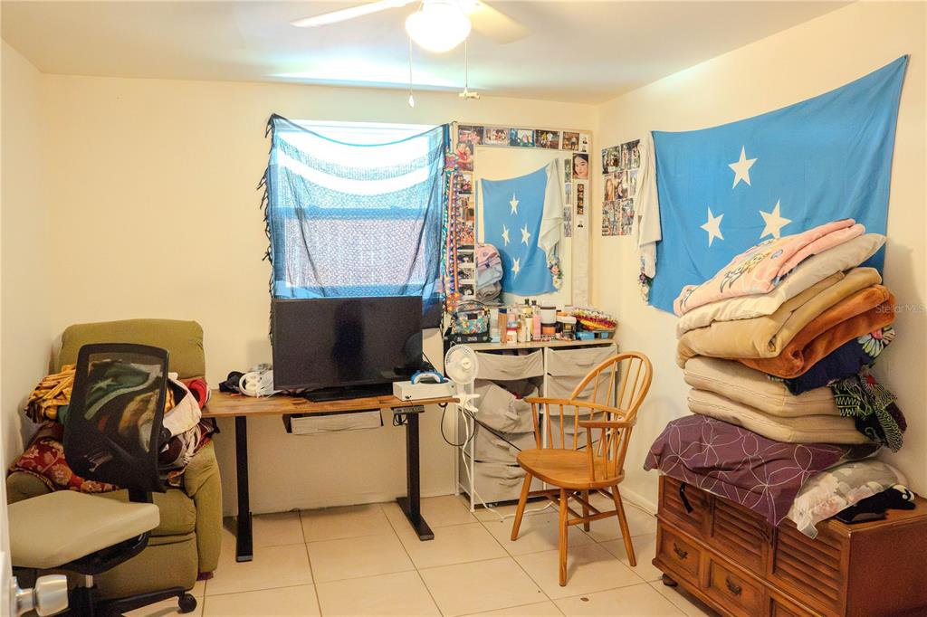 A bedroom features a desk with a television, a wooden chair, and a stack of bedding — 638 DOGWOOD COURT, DUNEDIN, FL