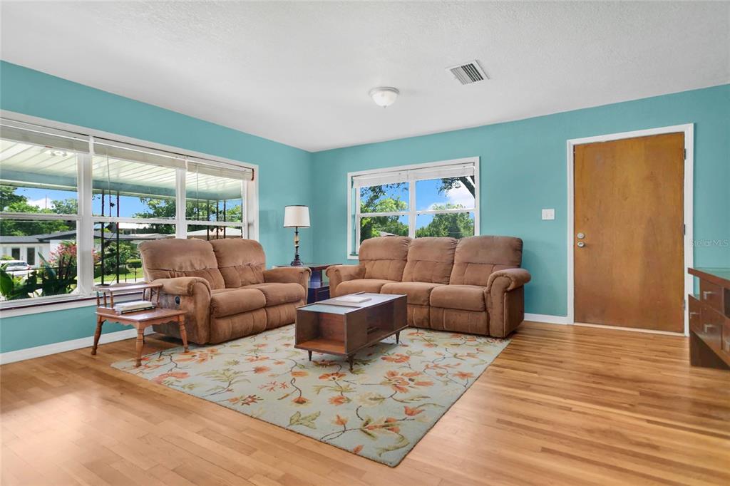 A living room features light blue walls, hardwood floors, a floral rug, and brown furniture — 2418 E JERSEY AVENUE, ORLANDO, FL
