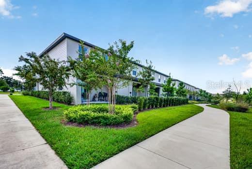 A multi-story residential building with a concrete walkway and landscaped lawn under a blue sky — 6119 SHINER STREET, LAND O LAKES, FL