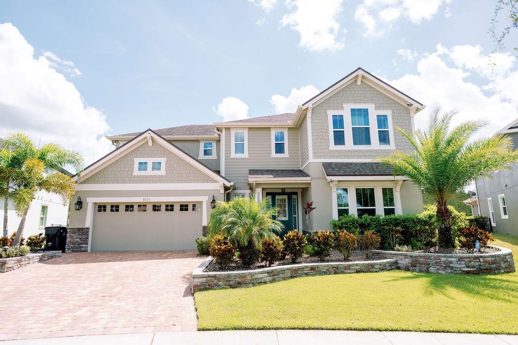 A two-story house with light-colored siding, a stone retaining wall, and a prominent palm tree — 8173 GAMEMASTER AVENUE, ORLANDO, FL