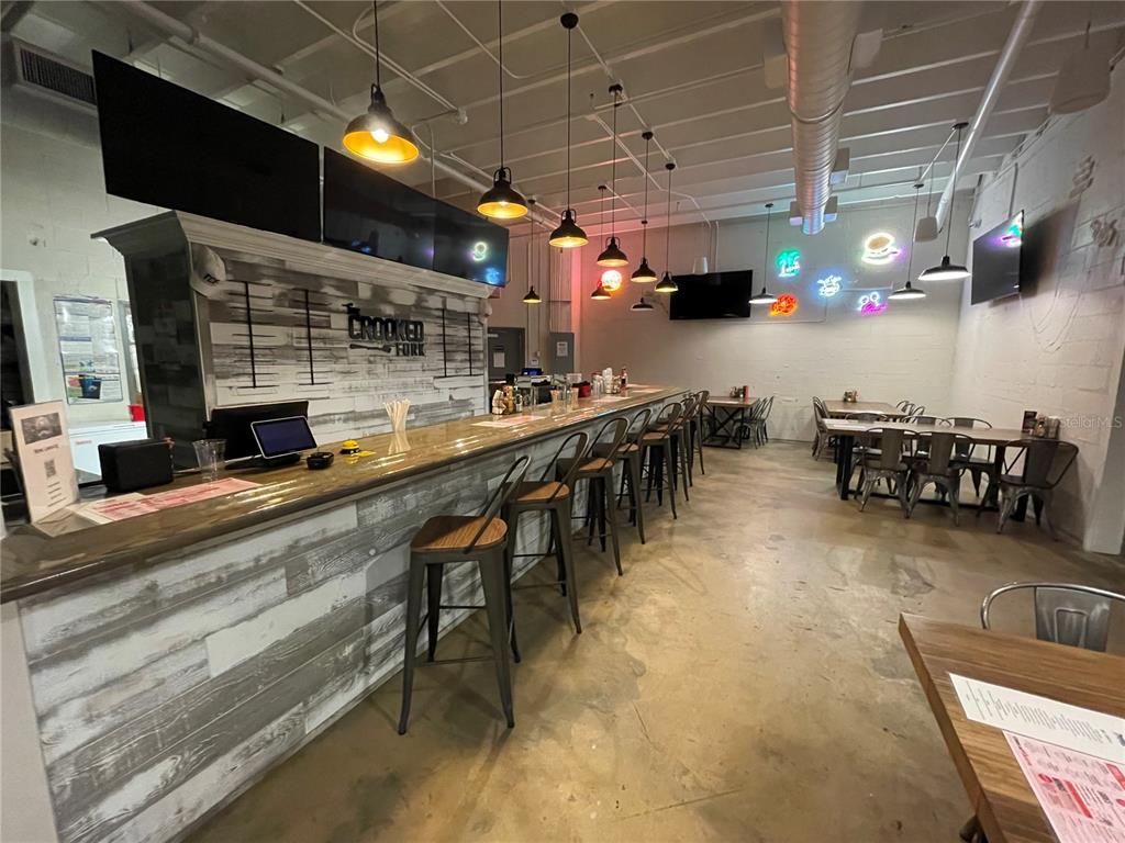A restaurant interior features a long bar with stools, pendant lighting, and casual dining tables — 24 E MAGNOLIA AVENUE UNIT 5, EUSTIS, FL