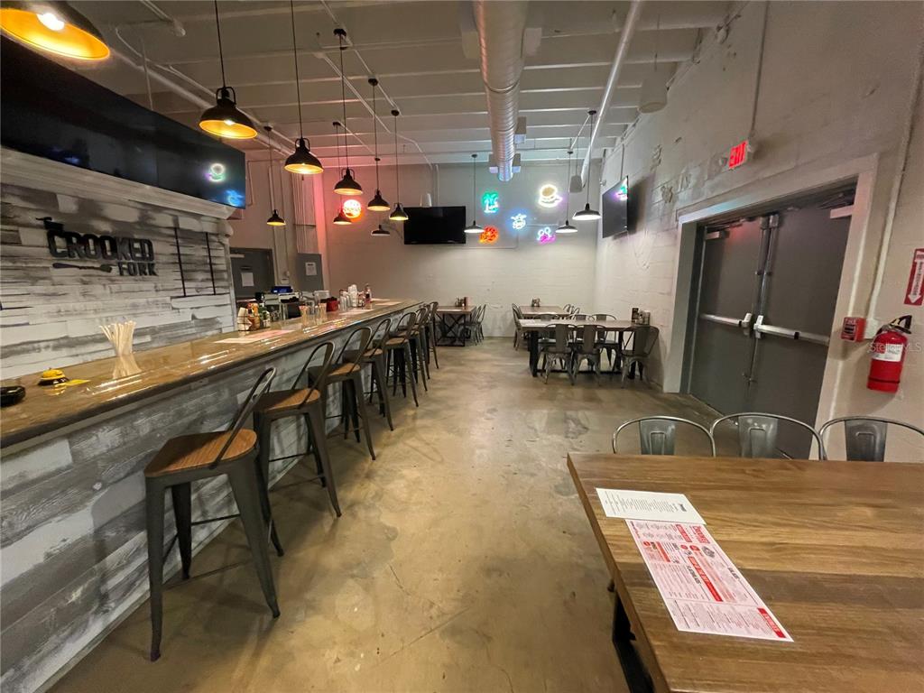 A restaurant interior features a long bar with stools, tables, and industrial-style lighting — 24 E MAGNOLIA AVENUE UNIT 5, EUSTIS, FL