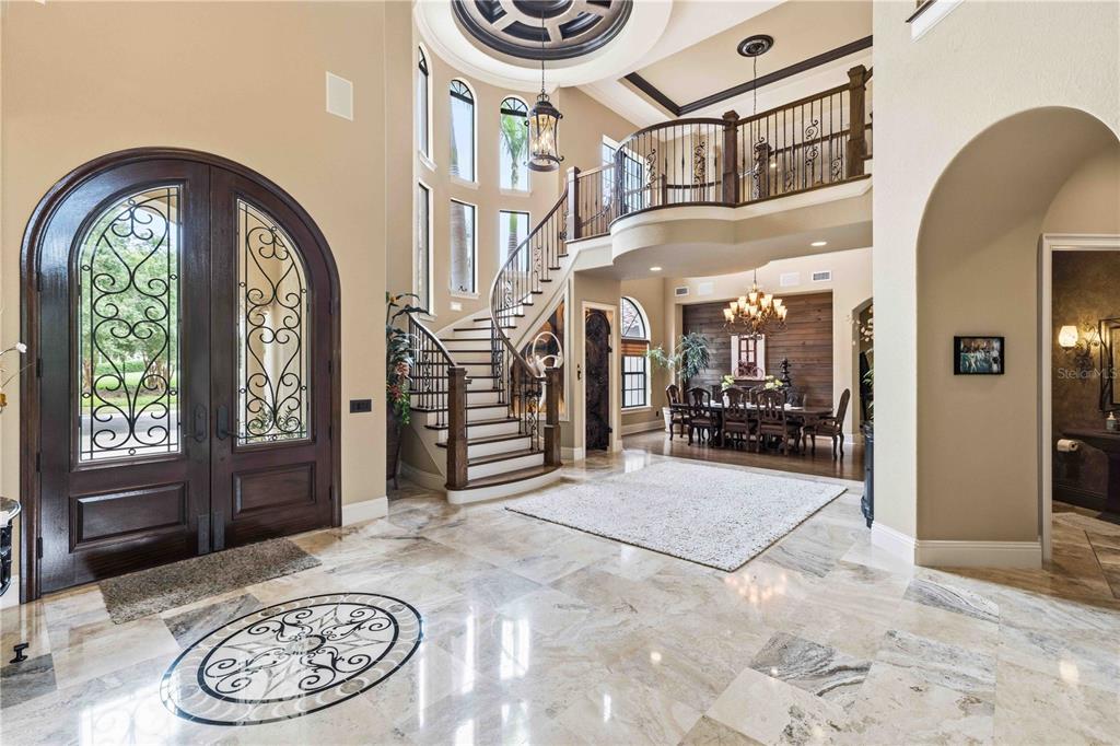 A grand foyer features a curved staircase, marble flooring, and a view into the dining room — 16220 TERNGLADE DRIVE, LITHIA, FL