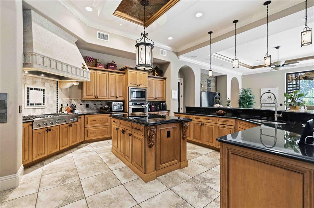 A kitchen features wood cabinets, black countertops, a central island, and tile flooring — 16220 TERNGLADE DRIVE, LITHIA, FL