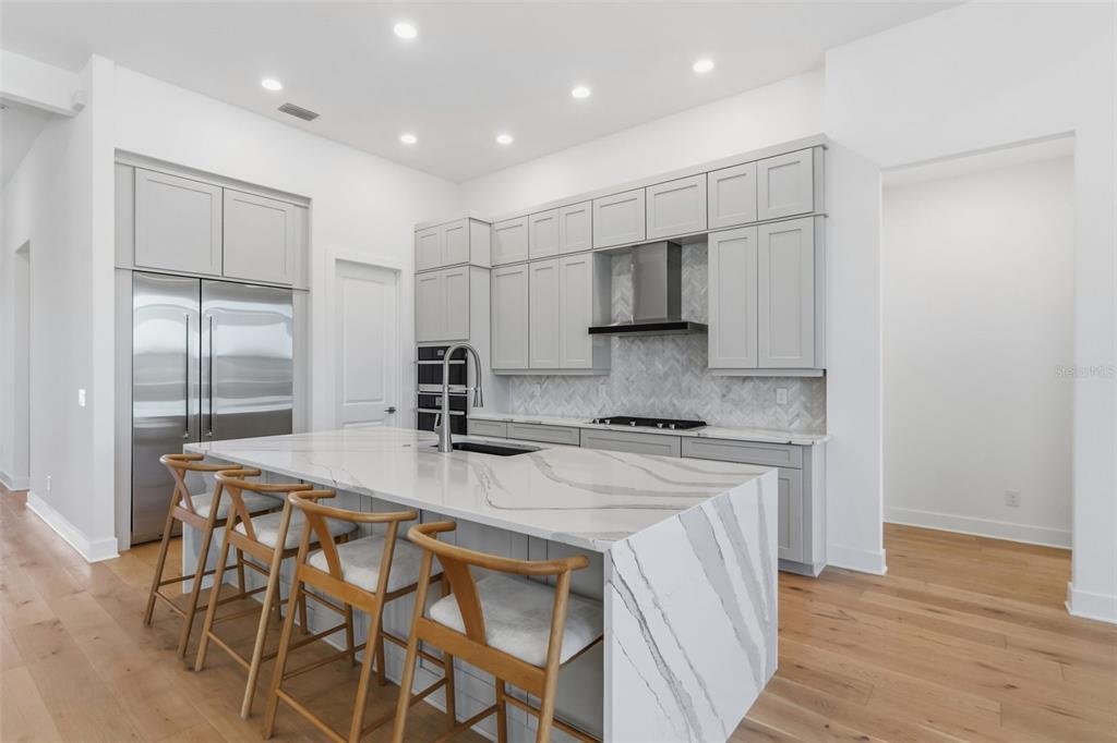 A modern kitchen features light gray cabinets, a marble waterfall island, and stainless steel appliances — 7982 REDONDA LOOP, BRADENTON, FL