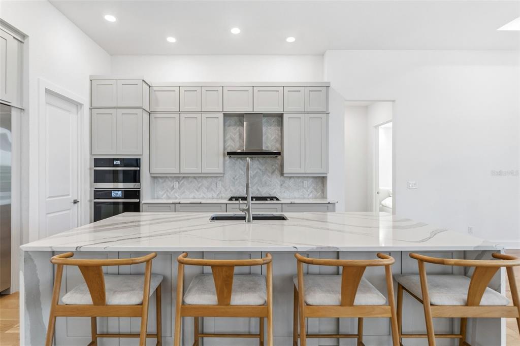 A modern kitchen features light gray cabinets, a marble-topped island, and four wooden bar stools — 7982 REDONDA LOOP, BRADENTON, FL