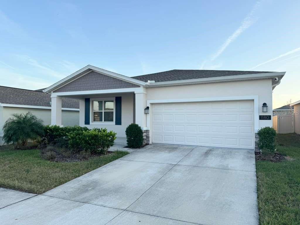 A single-story house with a white garage door, tan stucco siding, and a covered entryway — 1180 SAGUARO STREET, HAINES CITY, FL