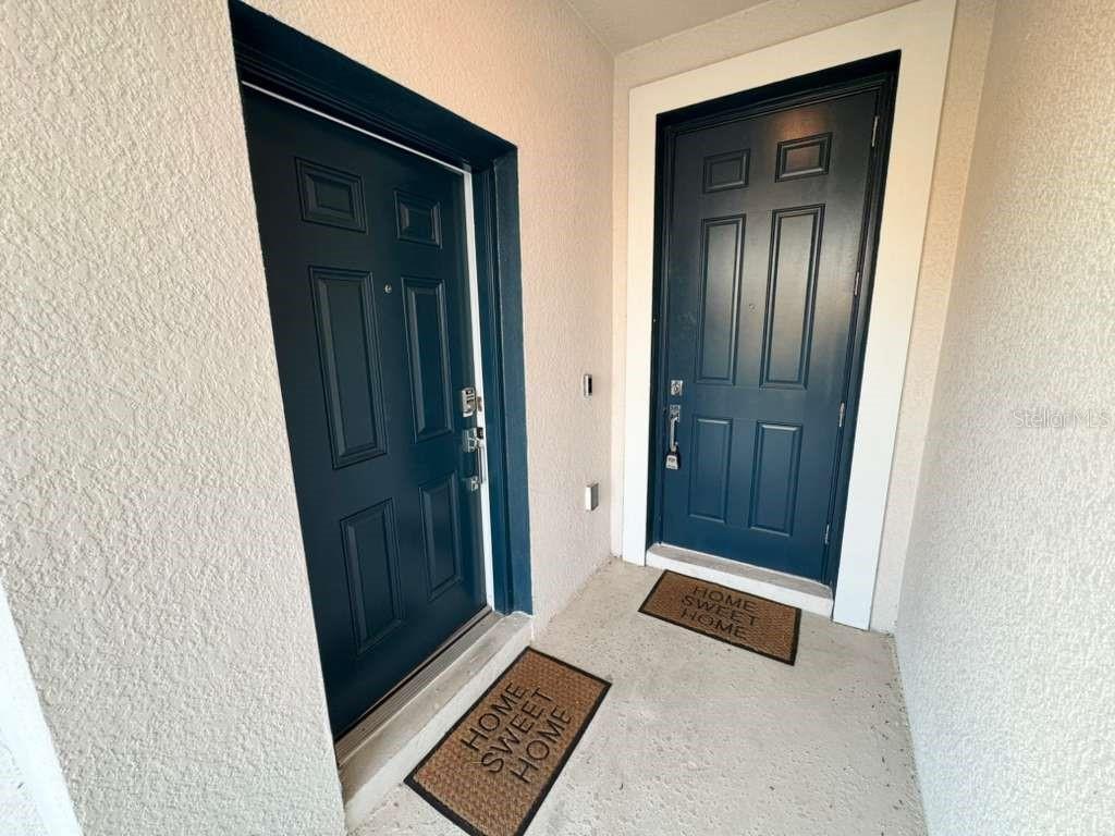 Two dark blue front doors with matching "Home Sweet Home" doormats in a recessed entryway — 1180 SAGUARO STREET, HAINES CITY, FL