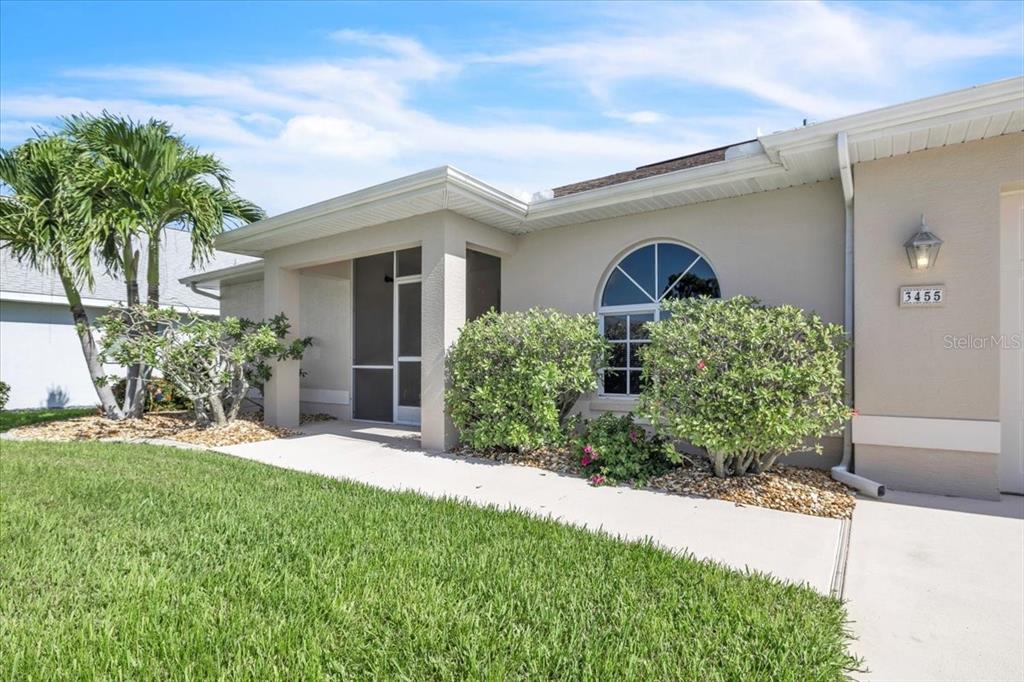 The exterior of a single-story house features a screened entryway, a lawn, and landscaping — 3455 SABAL SPRINGS BOULEVARD, NORTH FORT MYERS, FL