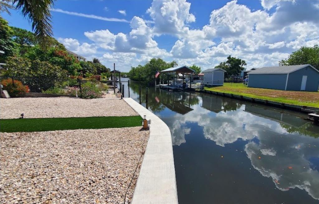 A gravel yard with a concrete seawall borders a canal featuring a boat lift — 3503 W SHELL POINT ROAD, RUSKIN, FL