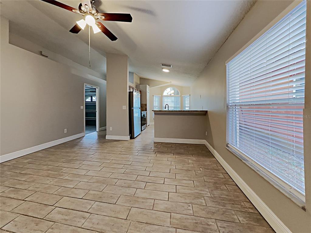 An open-concept room features light-colored tile flooring, a ceiling fan, and a kitchen pass-through window — 1604 CHATHAM CIRCLE, APOPKA, FL