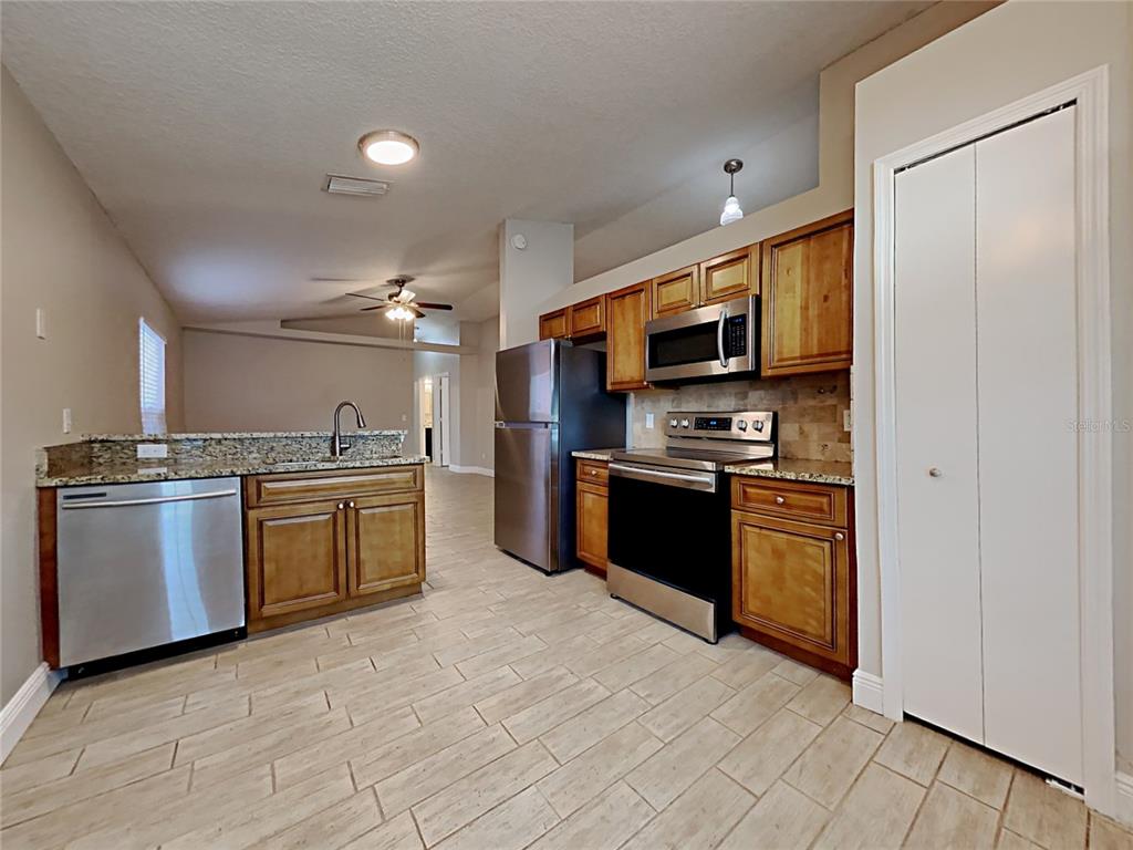 A kitchen features stainless steel appliances, wood cabinets, granite countertops, and light-colored tile flooring — 1604 CHATHAM CIRCLE, APOPKA, FL
