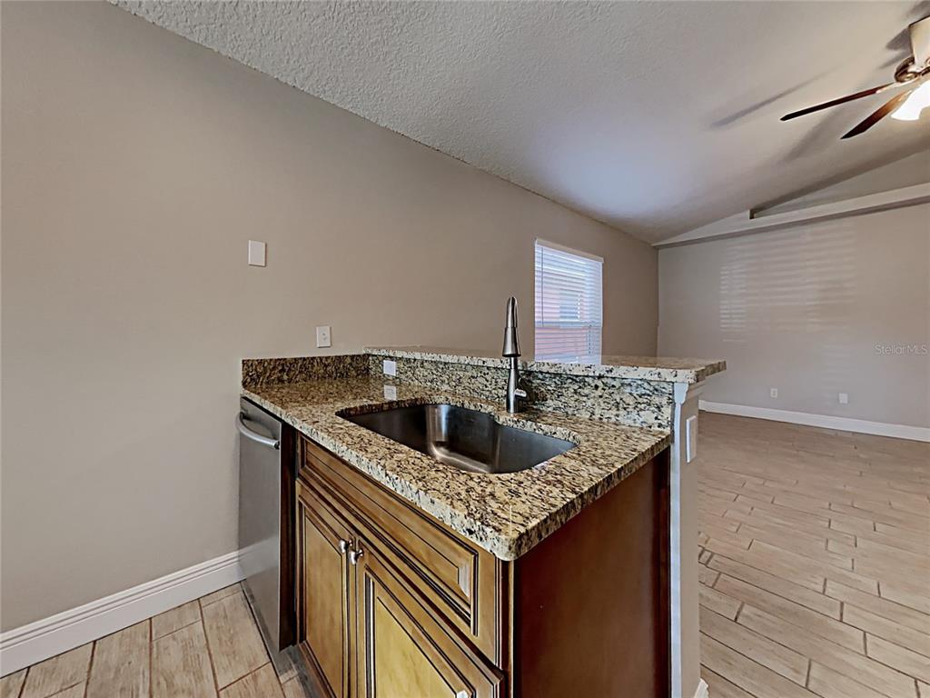 A kitchen sink with granite countertops and wooden cabinets overlooks an adjacent living area — 1604 CHATHAM CIRCLE, APOPKA, FL