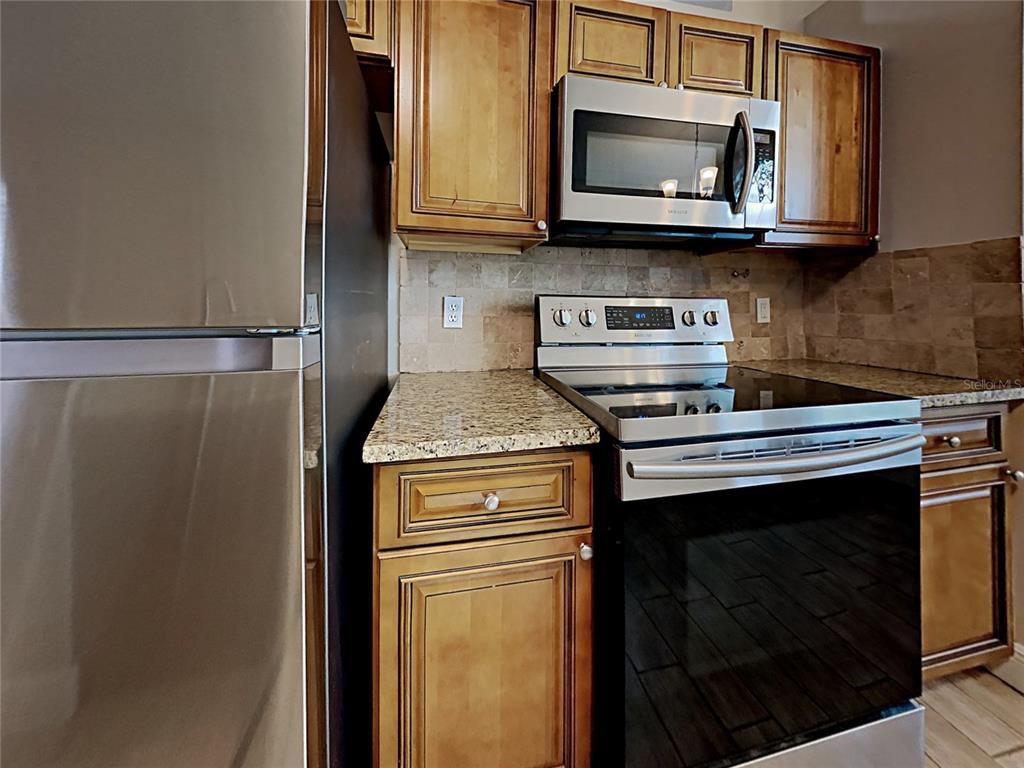 A kitchen features stainless steel appliances, wood cabinets, and granite countertops with a tiled backsplash — 1604 CHATHAM CIRCLE, APOPKA, FL