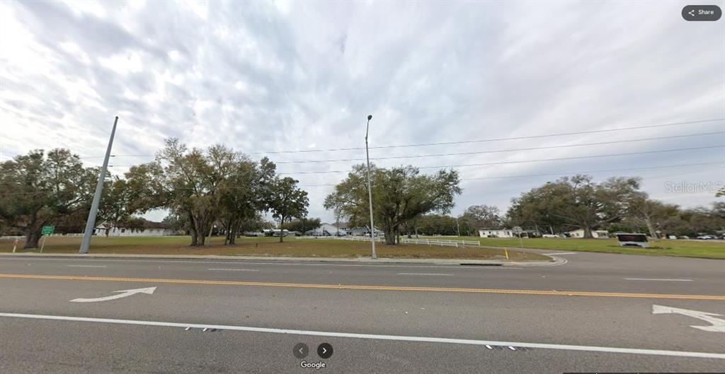 A wide, grassy vacant lot with several large trees sits alongside a paved road — N/A, KATHLEEN, FL