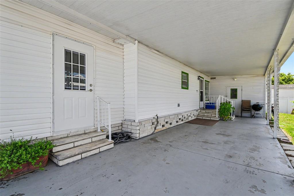 A white mobile home exterior features a concrete carport, two entry doors, and stone skirting — 3902 JULIE DRIVE, WESLEY CHAPEL, FL