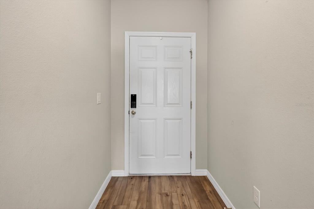 A white six-panel door with a smart lock stands at the end of a hallway — 14716 GALLOP RUN DRIVE, LITHIA, FL