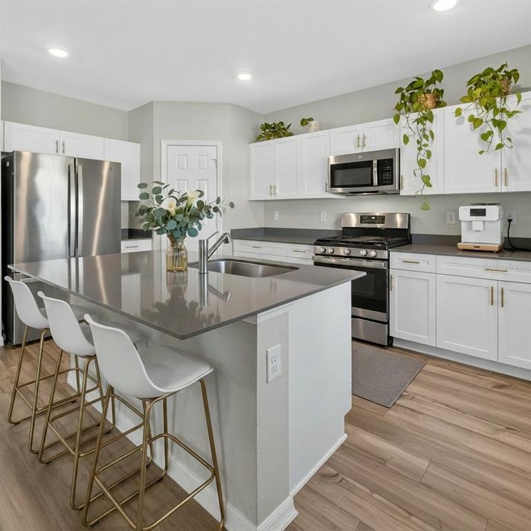 A kitchen with white cabinets, a gray island, stainless steel appliances, and wood-look flooring — 14716 GALLOP RUN DRIVE, LITHIA, FL