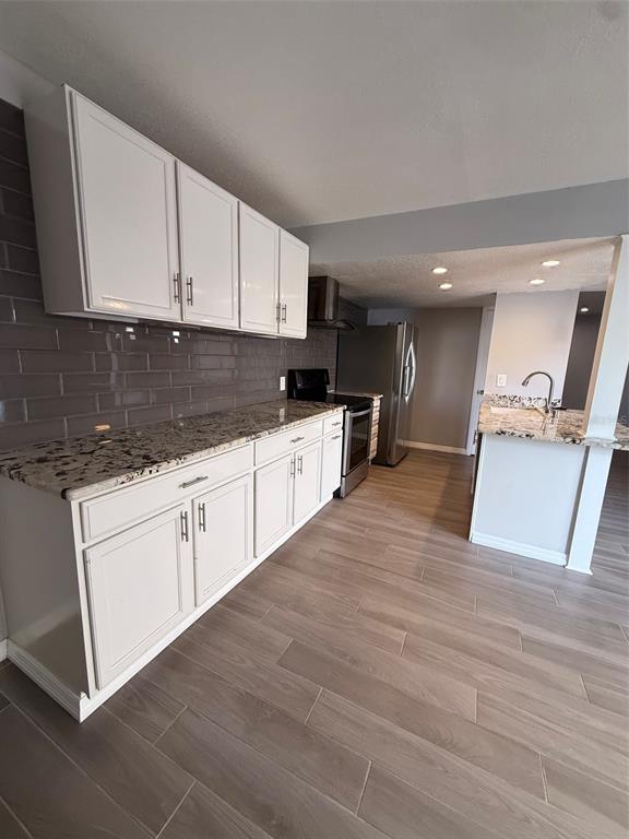 A kitchen features white cabinets, granite countertops, a gray subway tile backsplash, and wood-look flooring — 6814 WHITMAN PLACE UNIT 6814, SARASOTA, FL