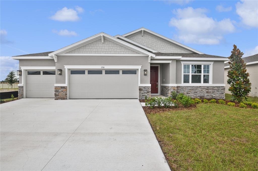 A single-story house features a gray stucco exterior, stone accents, and a three-car garage — 1718 CROOKED CREEK STREET, ST CLOUD, FL