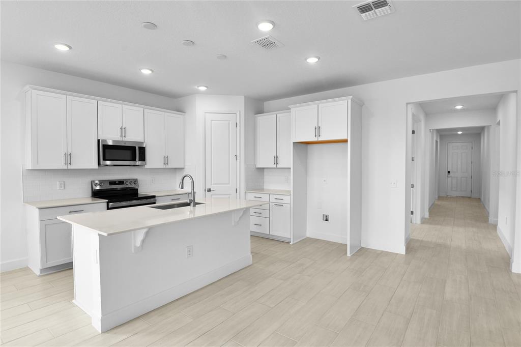 A modern kitchen features white cabinetry, a central island with a sink, and light tile flooring — 1718 CROOKED CREEK STREET, ST CLOUD, FL