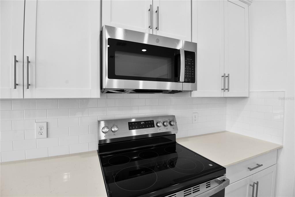 A kitchen features white cabinets, a stainless steel microwave, and a black electric range — 1718 CROOKED CREEK STREET, ST CLOUD, FL