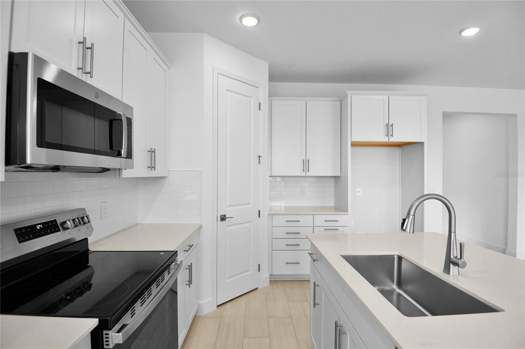 A modern kitchen features white cabinetry, stainless steel appliances, a center island, and light flooring — 1718 CROOKED CREEK STREET, ST CLOUD, FL